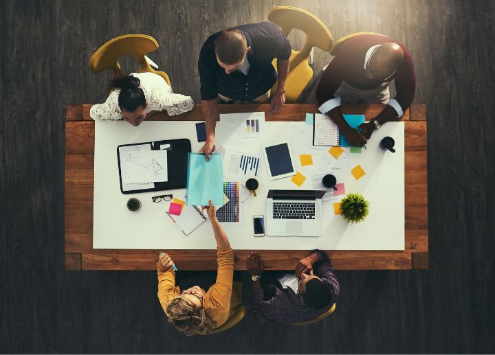 Overhead view of people gathered around a table collaborating with laptops, documents, and notes